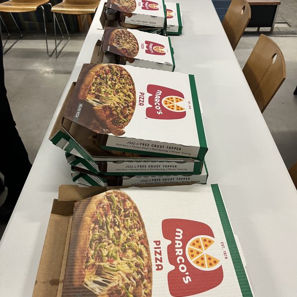 Several large pizza boxes arranged on long tables inside a police district break room, prepared for a meal.