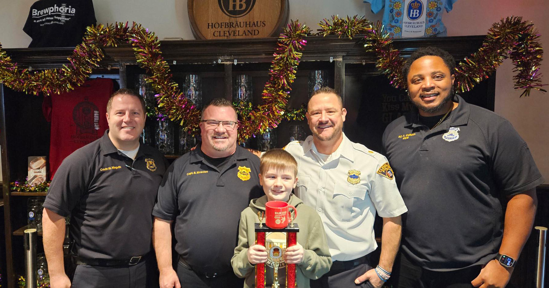 Cleveland Police officers pose with a young boy holding the Chili Bowl Classic trophy inside Hofbräuhaus Cleveland