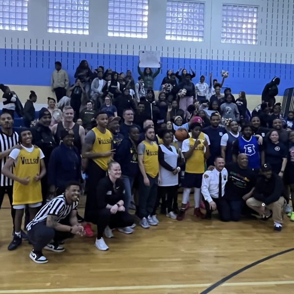Both teams and officials pose together on the court with a packed crowd of Willson School supporters in the bleachers behind them