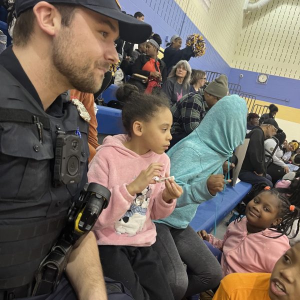 A Cleveland Police officer sits in the bleachers alongside young students during the game