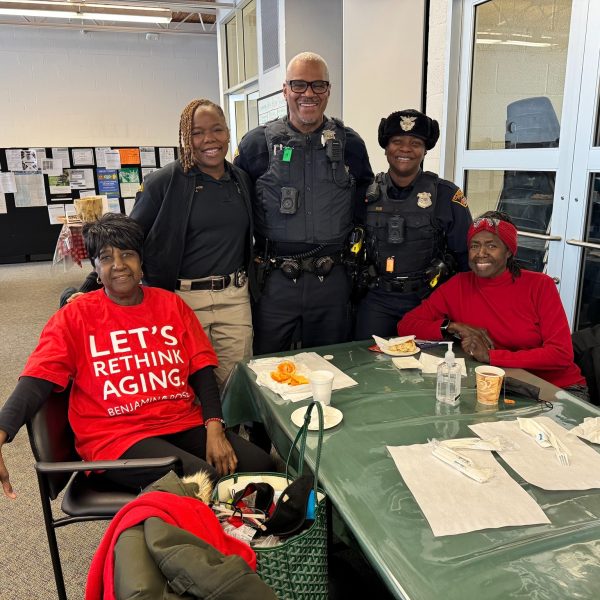 Two Cleveland Police officers pose with two community members seated at a table, one wearing a Benjamin Rose t-shirt