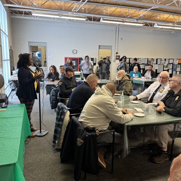 A speaker addresses a room of officers and community members at a microphone during the Coffee with a Cop event at Gunning Recreation Center
