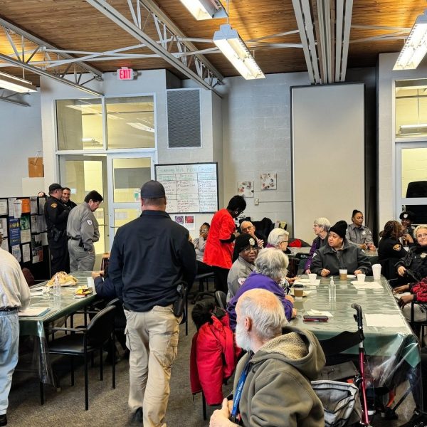 Officers and community members mingle at tables during the Coffee with a Cop event, with a Gunning Rose Center schedule board visible on the wall