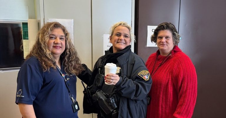 A Cleveland Police officer holds a coffee cup while posing with two staff members inside Gunning Recreation Center