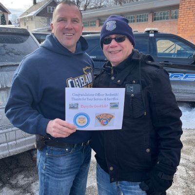 Officer Paul Beckwith and a colleague hold a congratulatory card outside the Second District following his retirement sendoff